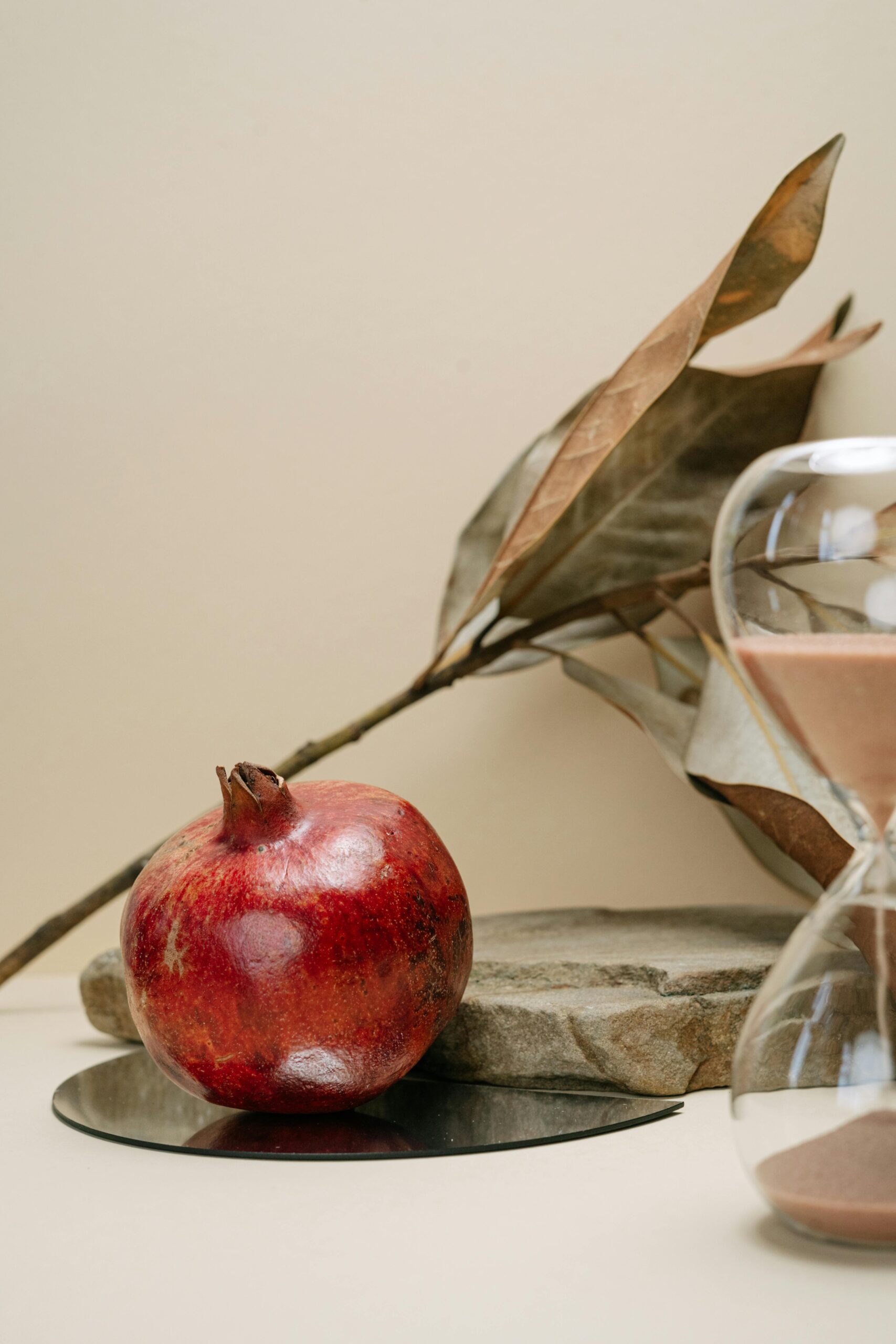laurette naturopathe les 3 piliers de la naturopathie image d une nature morte avec une grenade un sablier, une pierre plate et une branche de laurier sèche en arrière plant